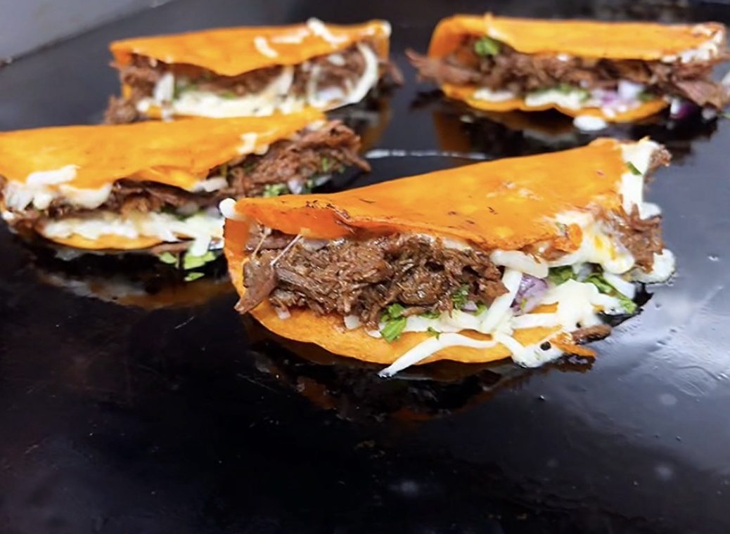 Guat-A-Taco quesabirria tacos on the griddle — crispy orange corn tortillas filled with slow-braised birria beef, melted cheese, cilantro, and onion